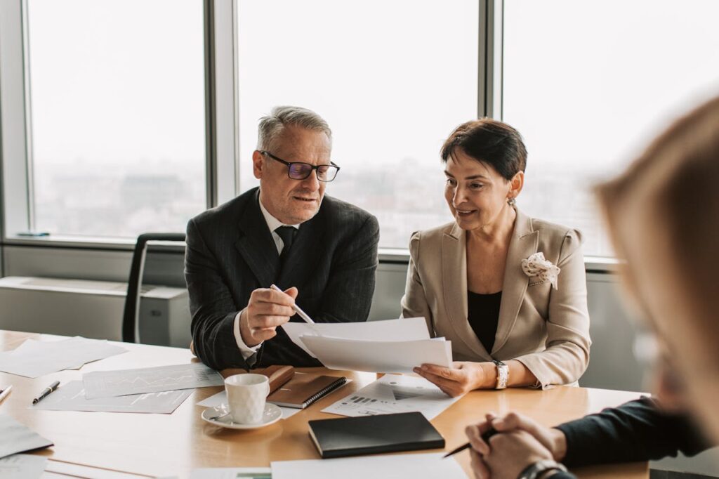 Senior business professionals discussing documents in a corporate office setting.